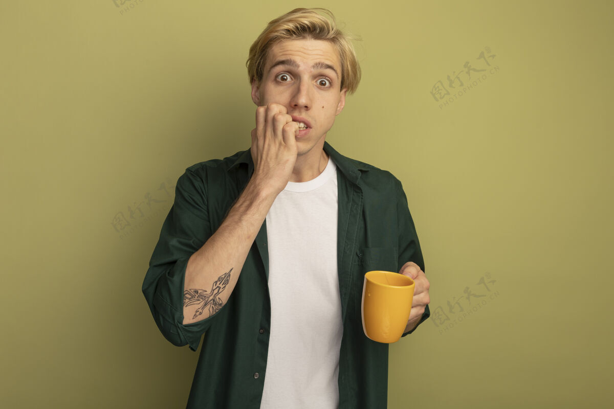 年轻一个穿着绿色t恤 端着一杯茶 咬着指甲的年轻金发男人小伙子茶帅哥