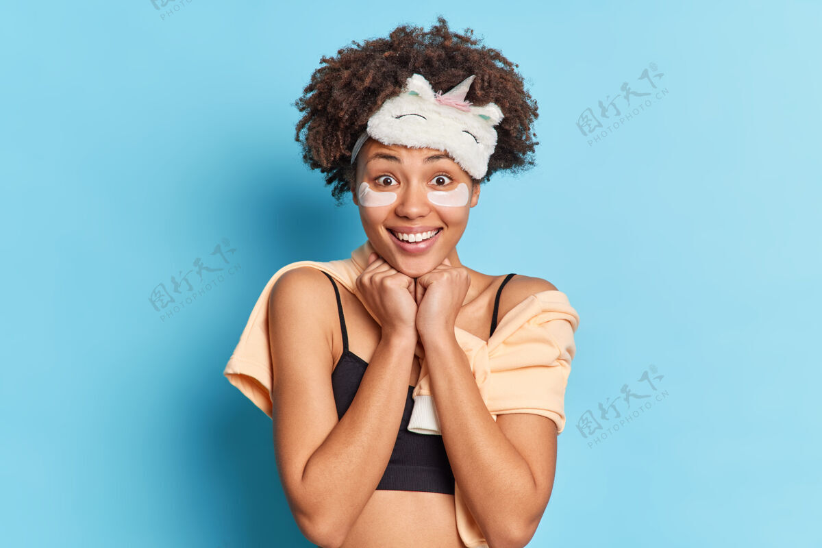 请积极的黑皮肤女人留着非洲头发 手放在下巴下面 直视镜头蓝色睡眠卷发