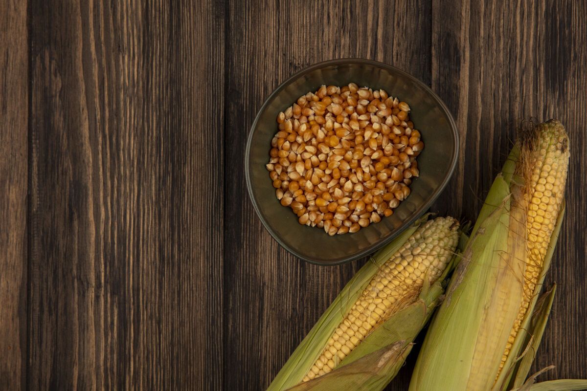 玉米顶视图的有机和新鲜的玉米与头发与玉米粒在一个碗上的木桌与复制空间果仁顶部玉米