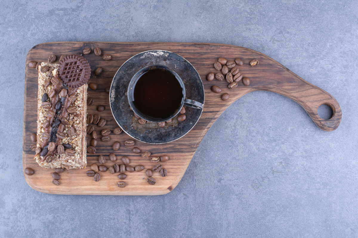 早餐一块蛋糕和咖啡豆旁边的一杯咖啡放在大理石表面的木板上咖啡因饼干咖啡