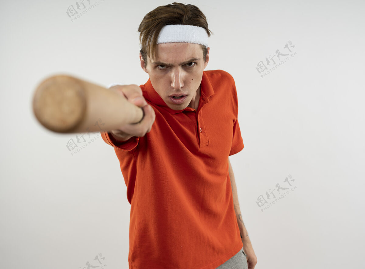 严格严格的年轻运动男子戴着头带与手腕举行棒球棒隔离在白墙上棒球抱着头带