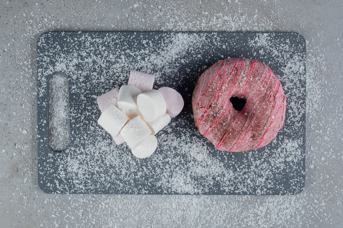 辛辣一堆棉花糖和一个甜甜圈放在椰子粉覆盖的大理石板上糖可口美味