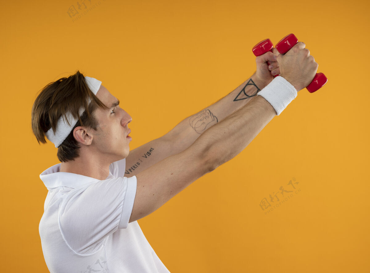 运动站在侧视图中的年轻运动型男子戴着头带和腕带 在黄色墙壁上孤立着哑铃练习腕带穿头带