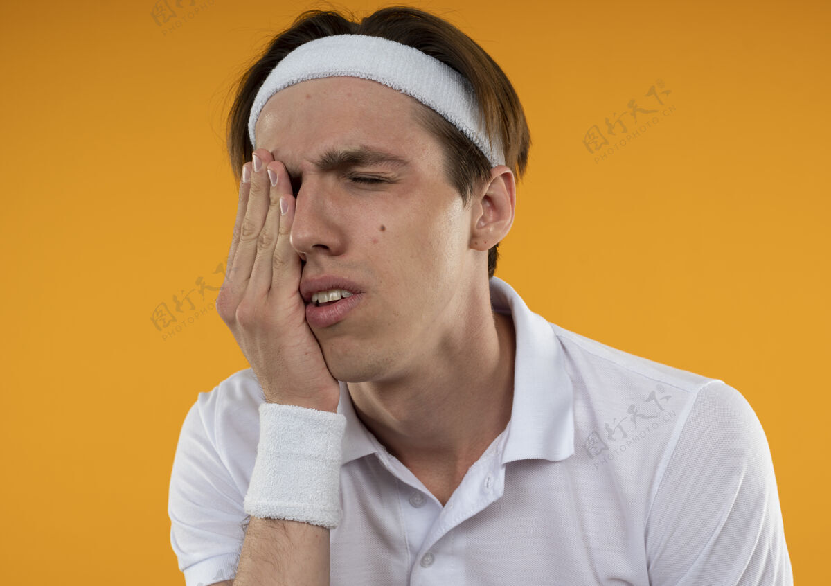 家伙一个不快乐的年轻人 闭着眼睛 戴着头带和腕带 手放在眼睛上 被隔离在橙色的墙上腕带封闭不愉快