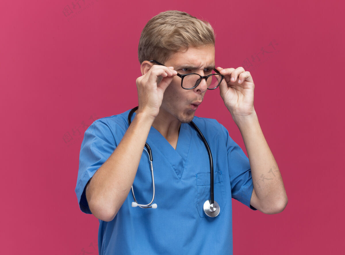 年轻惊讶地看着旁边穿着医生制服的年轻男医生 听诊器和眼镜被隔离在粉红色的墙上听诊器眼镜男性