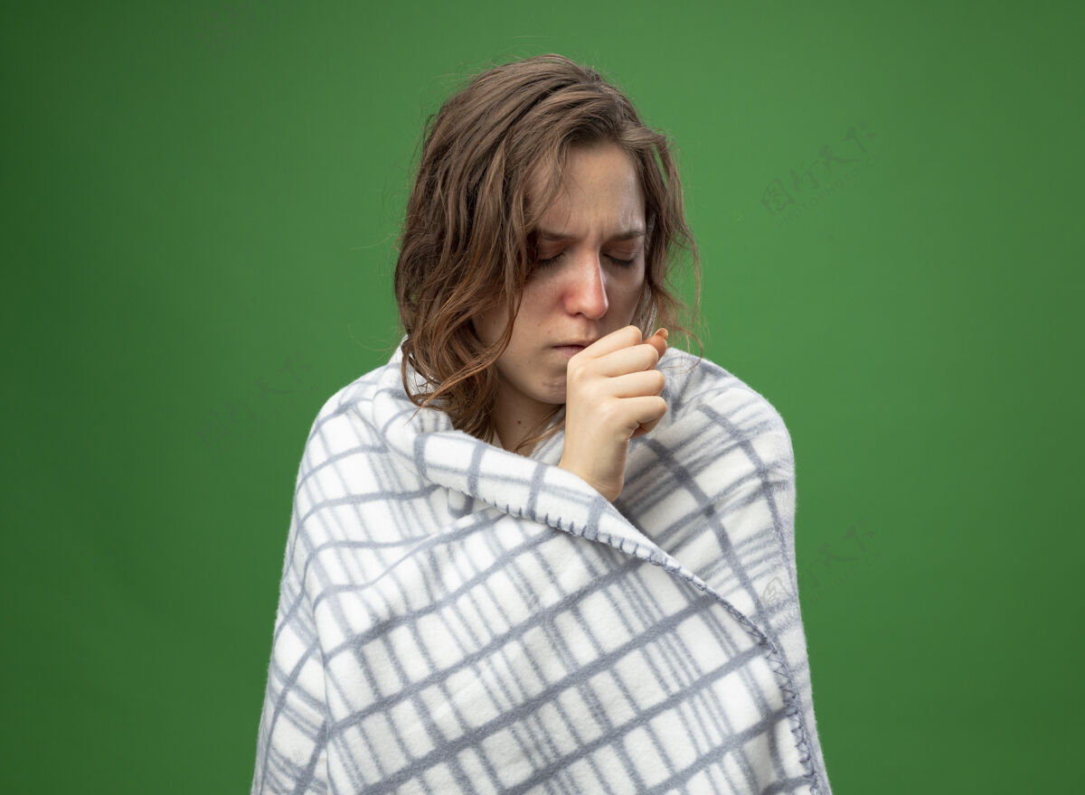持有咳嗽的年轻生病的女孩穿着白袍裹着格子布 手放在嘴上 嘴上隔离着绿色疾病年轻穿