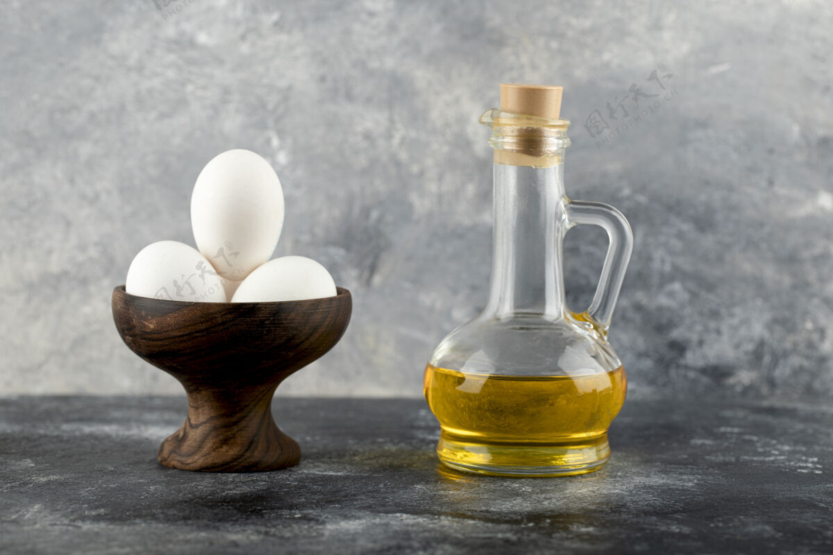 天然在大理石表面放一碗白鸡蛋和一瓶油生的烹饪玻璃