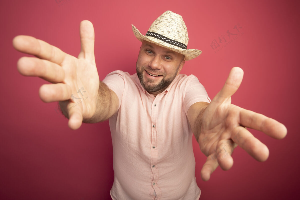 中年微笑的中年秃头男子身穿粉色t恤 戴着帽子举起双手孤立在粉色上手男人手