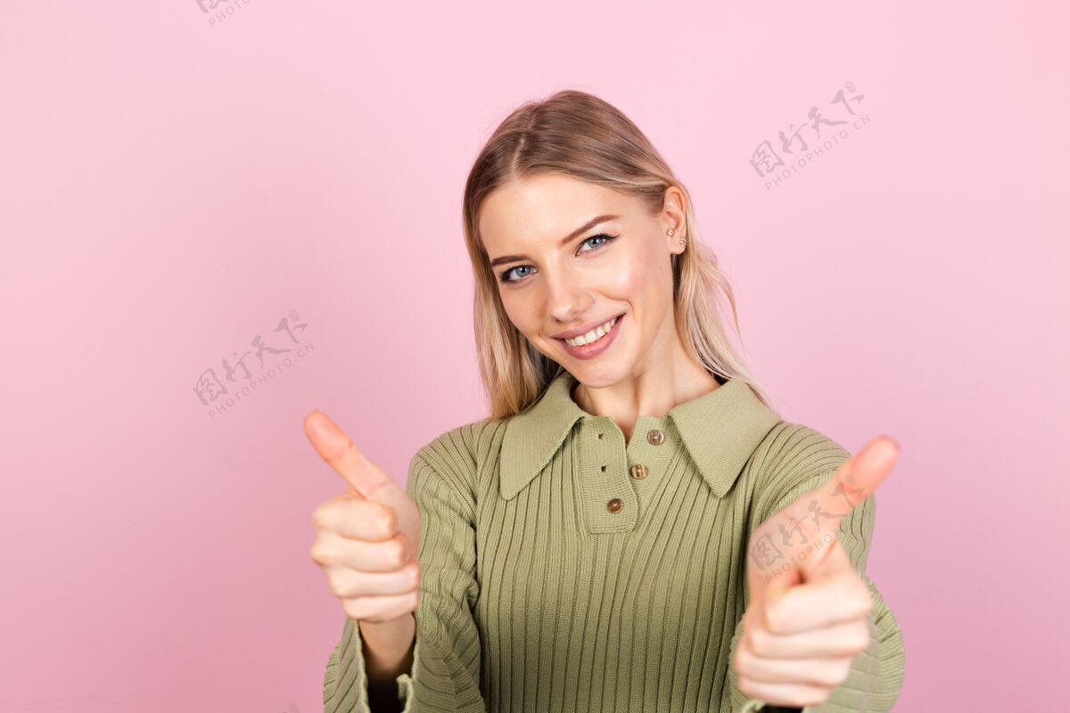 惊人粉色墙上穿着休闲毛衣的漂亮欧洲女人展示成功休闲