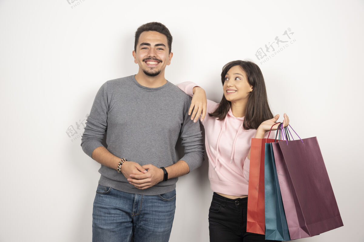 抱着一对年轻夫妇拿着购物袋站在白色的地板上夫妇女人人