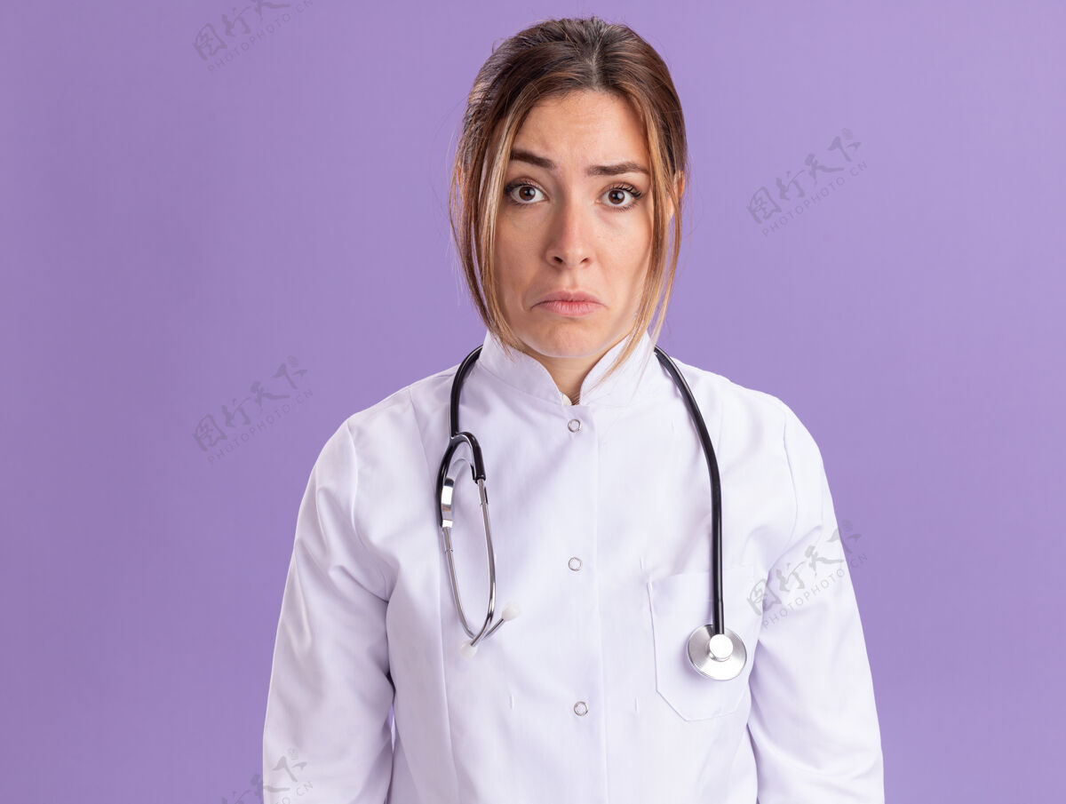 悲伤悲伤的年轻女医生穿着医用长袍 听诊器被隔离在紫色的墙上长袍女性医生