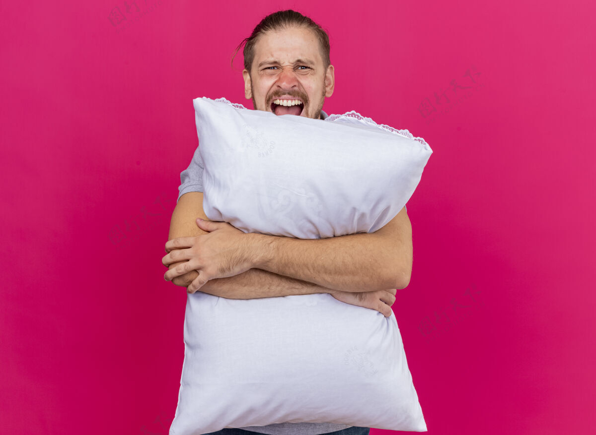 人愤怒的年轻英俊的斯拉夫病夫抱着枕头看着前面尖叫着隔离在粉红色墙上的复制空间枕头斯拉夫尖叫