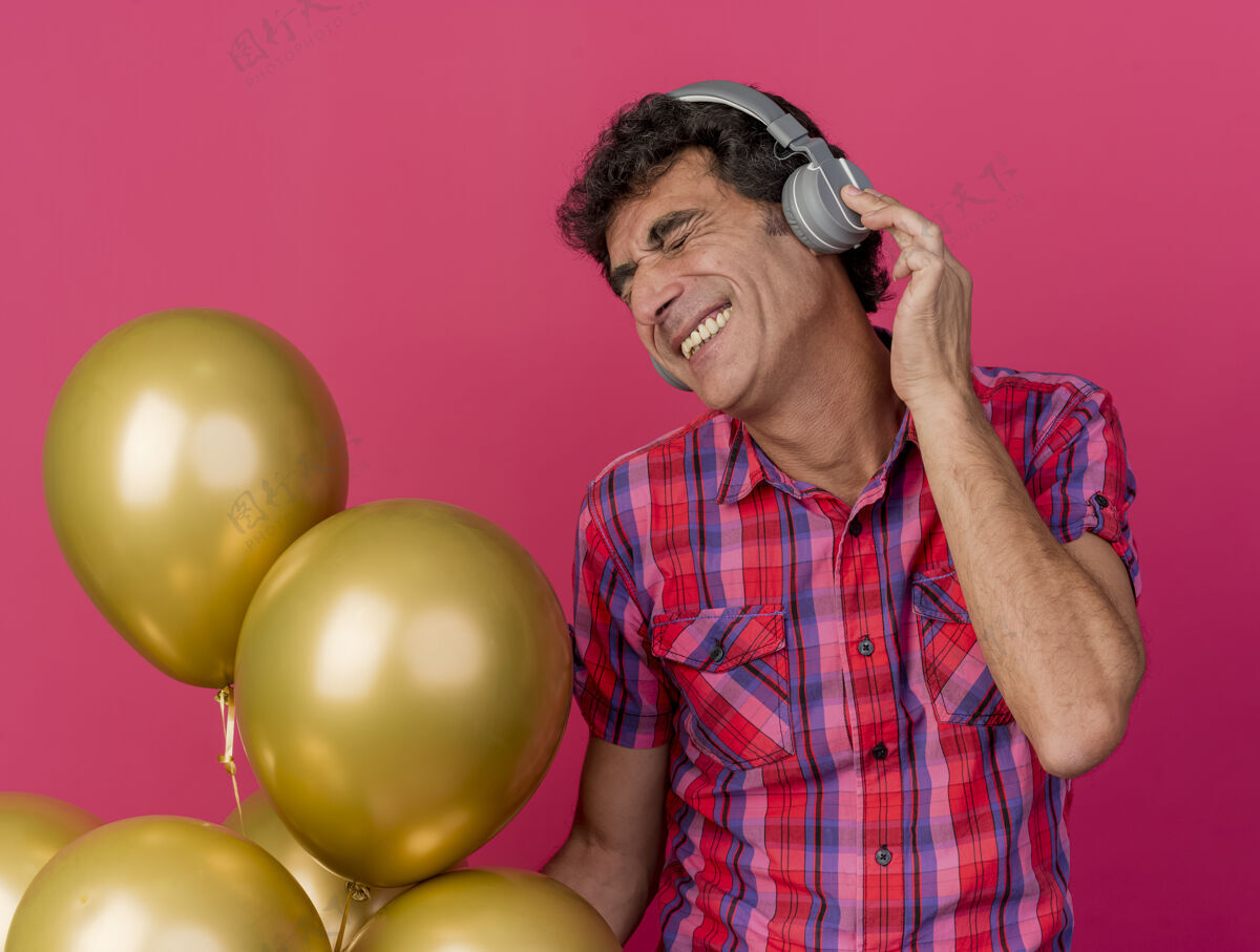 穿着微笑的中年派对男子戴着耳机拿着气球听着音乐闭着眼睛隔离在粉红色的墙上眼睛衣服感觉