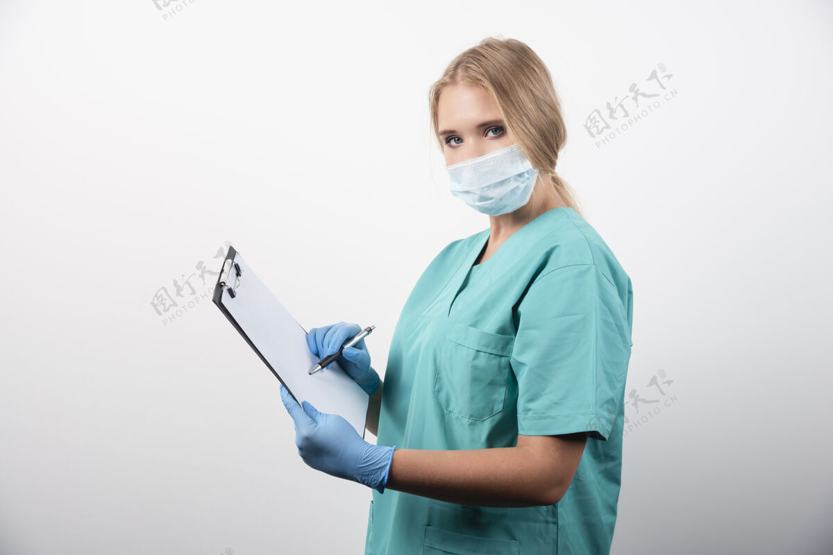 人女医生在剪贴板上写字 戴着医用口罩高质量的照片防护人女孩