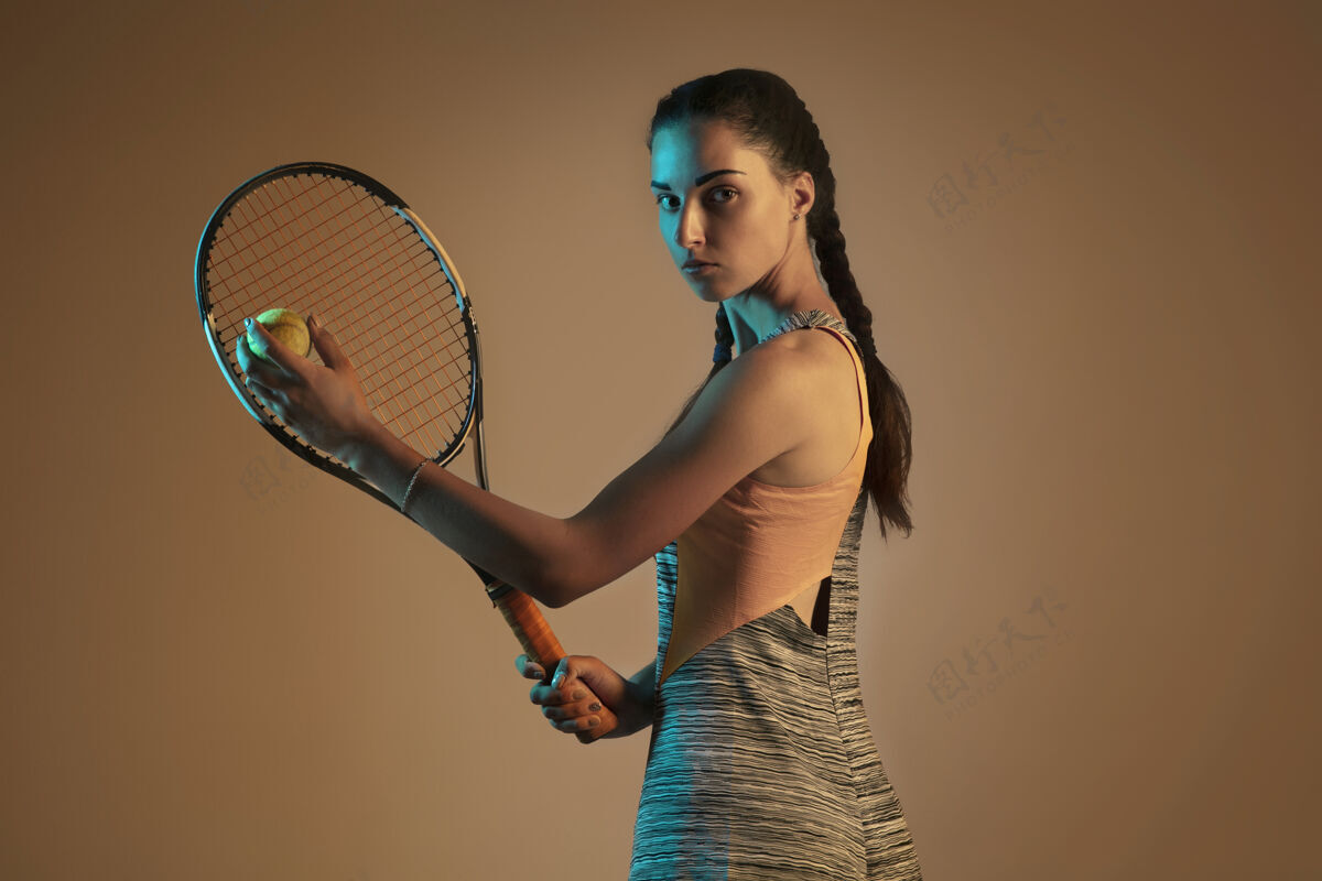 摄影棚射击一位白人女子在混合霓虹灯下孤立地打网球 背景是棕色适合年轻女性运动员在运动比赛中运动或动作运动 运动 健康生活方式的概念完整活动活动
