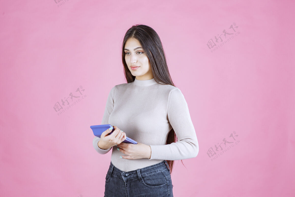 收入穿着灰色衬衫的女孩拿着一个蓝色的计算器 看着它 用它工作姿势会计休闲