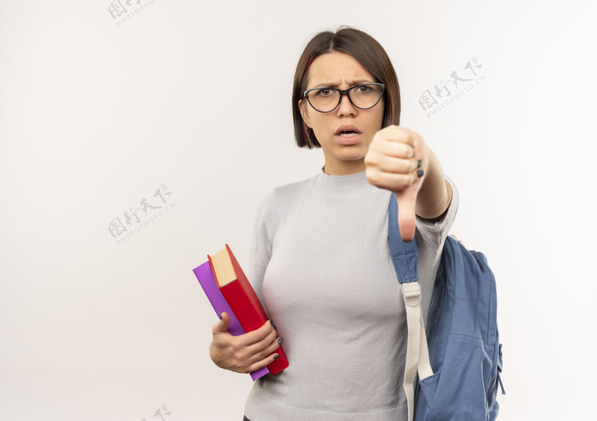 包未出租的年轻女学生戴着眼镜 背着书包 拿着书 大拇指朝下 在白色背景上 有复印空间拿着学生背