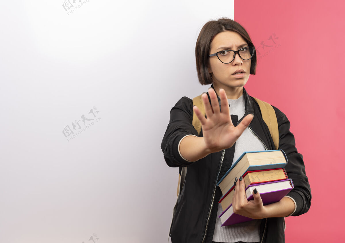 站一个戴着眼镜 背着书包 站在白色墙壁前的未出柜的年轻女学生 在粉色背景上用复印空间做着不孤立的手势学生背年轻