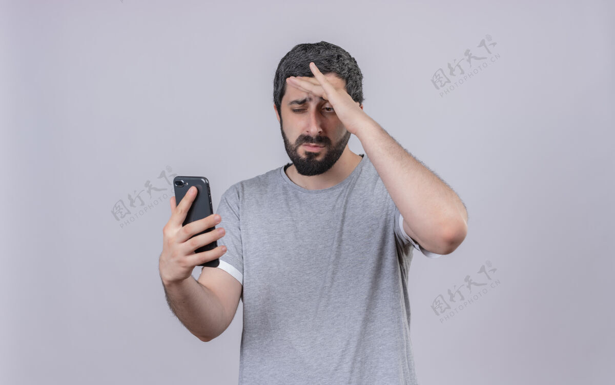 电话一个年轻英俊的白种人 手放在额头上 拿着手机 看着手机 背景是白色的 有复印空间额头年轻手机