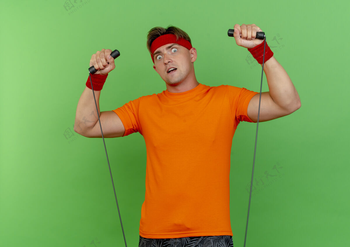 年轻印象深刻的年轻英俊的运动男子戴着头带和手腕拉着跳绳隔离在绿色绳子拉英俊