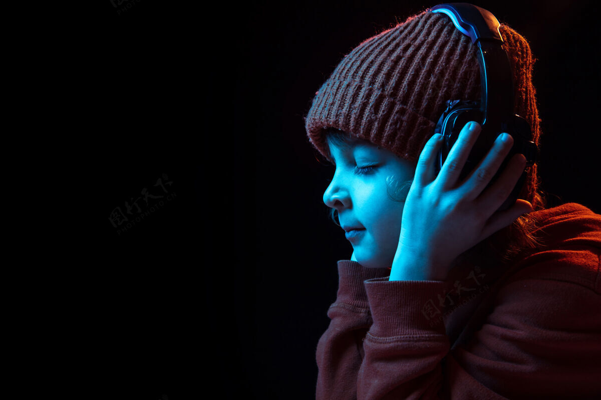 人戴着耳机 闭着眼睛 愉快地听着音乐霓虹灯下深色背景上的白人男孩肖像人类情感的概念 面部表情 销售 广告 现代科技 小玩意平板电脑使用显示