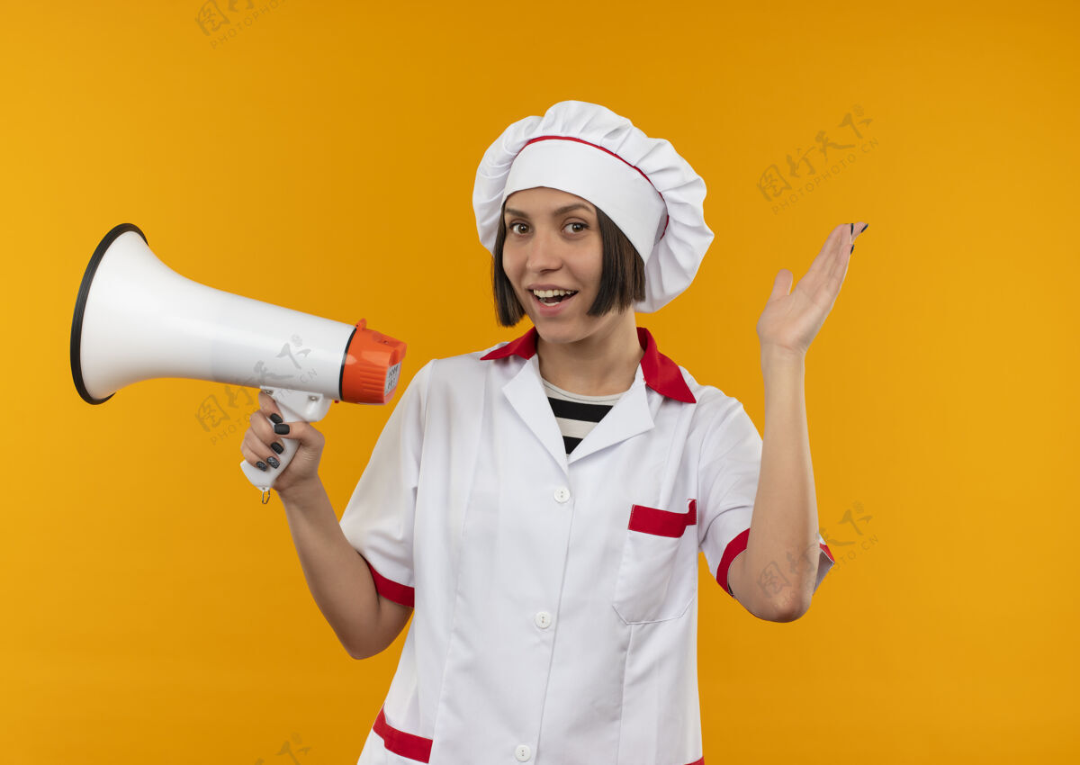 烹饪快乐的年轻女厨师 身着厨师制服 手举喇叭 手上空空的橘子色厨师扬声器欢乐