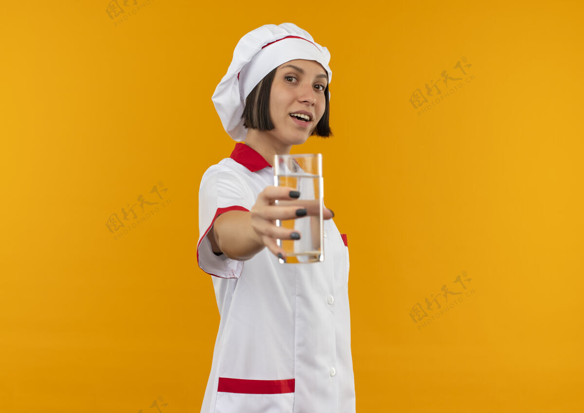 女快乐的年轻女厨师穿着厨师制服 伸出一杯橘子汁走向伸展年轻