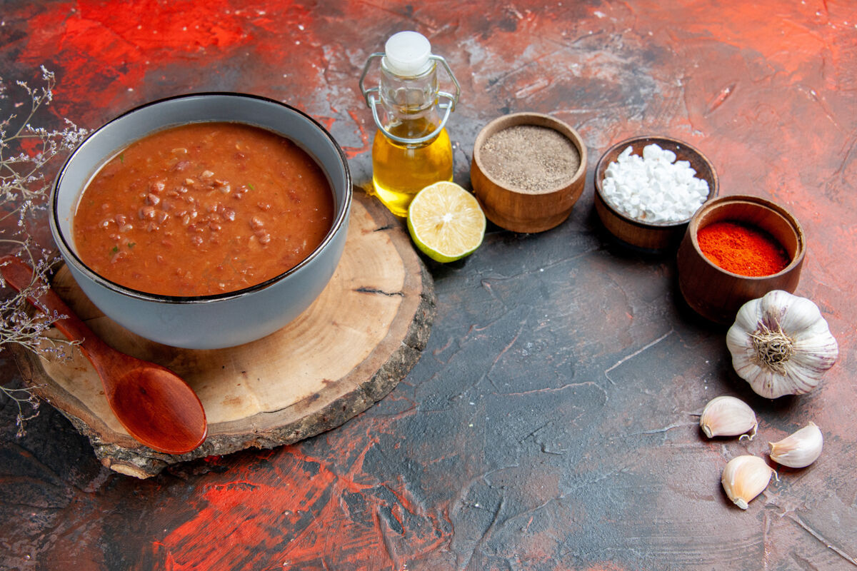 托盘木制托盘上的经典番茄汤的侧视图不同的香料和油瓶柠檬蒜放在五颜六色的桌子上木头柠檬碗