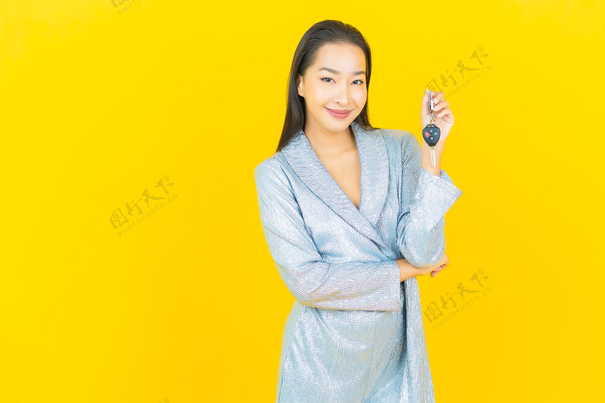 女孩画像美丽的亚洲年轻女子微笑着把车钥匙放在黄色的墙上微笑汽车成人
