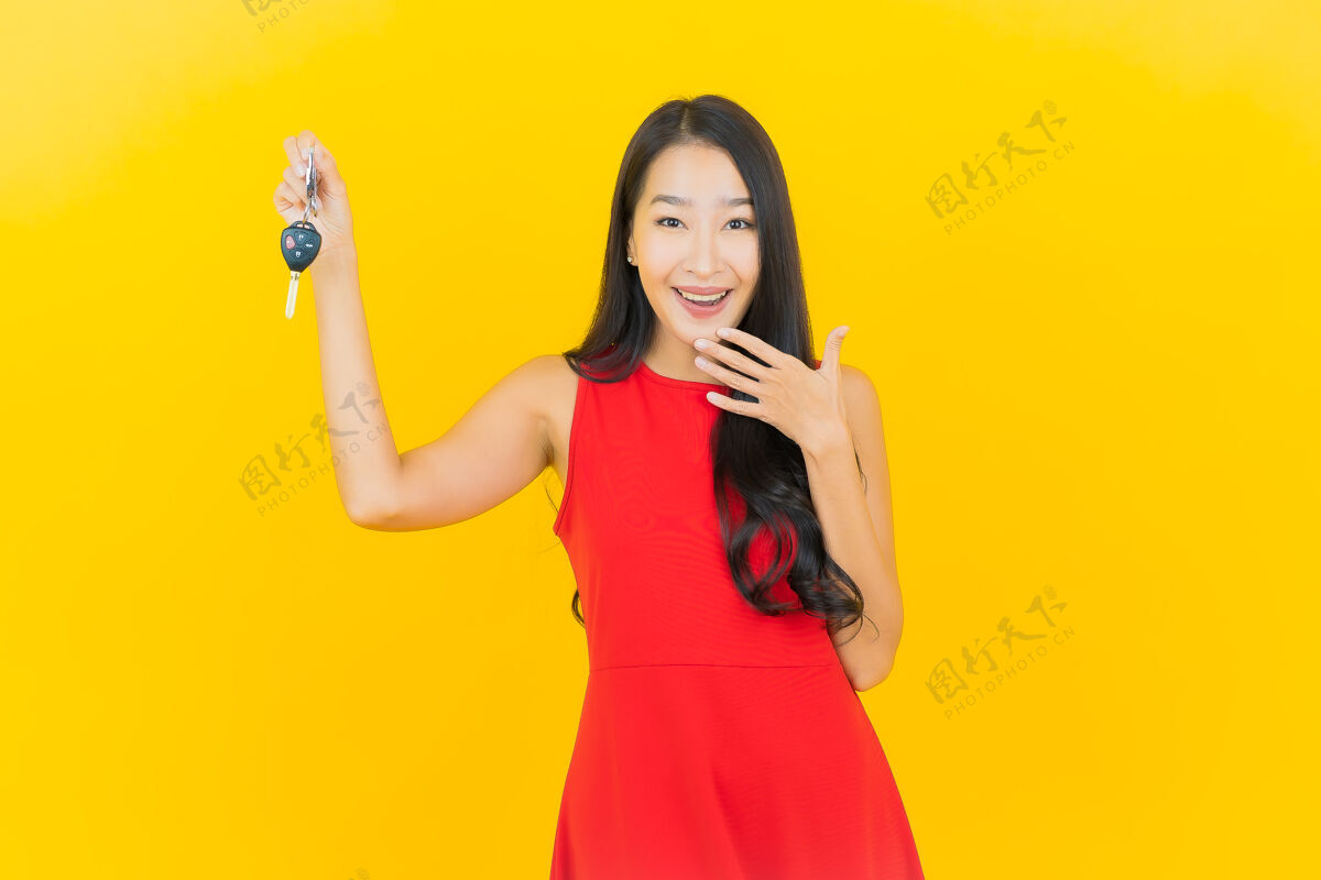 展示画像美丽的亚洲年轻女子微笑着把车钥匙放在黄色的墙上女性零售司机