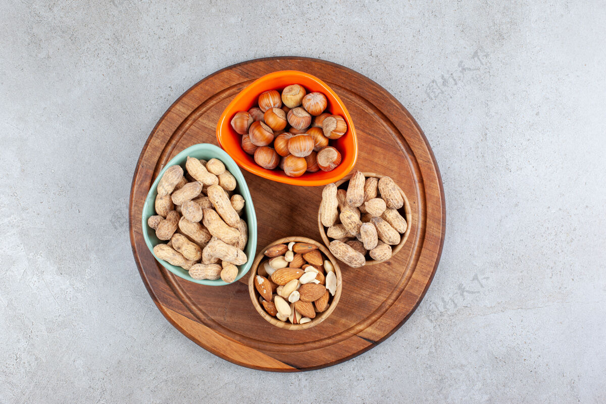健康在大理石背景的木制托盘上 各种不同的坚果被分到几个碗里高质量的照片美味榛子碗