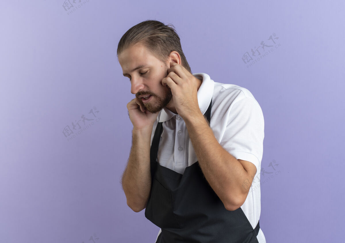 穿着穿着制服的年轻英俊的理发师把手指放在耳朵里闭着眼睛孤立在紫色背景上 留着复印空间耳朵眼睛帅气