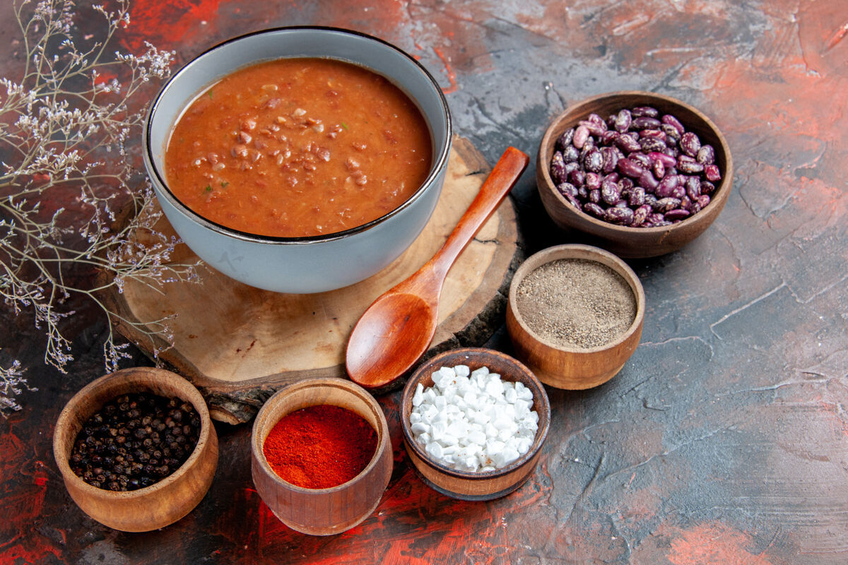 木头番茄汤用勺子放在木托盘上 豆子和不同的香料放在五颜六色的桌子上食物豆子姜黄