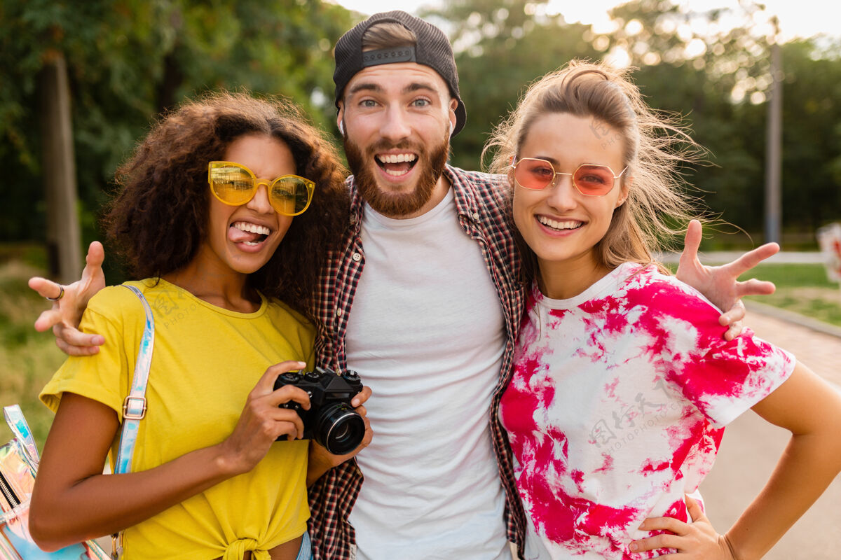 女性快乐的年轻朋友们带着相机在公园里散步 男女一起玩得很开心黑人人墨镜