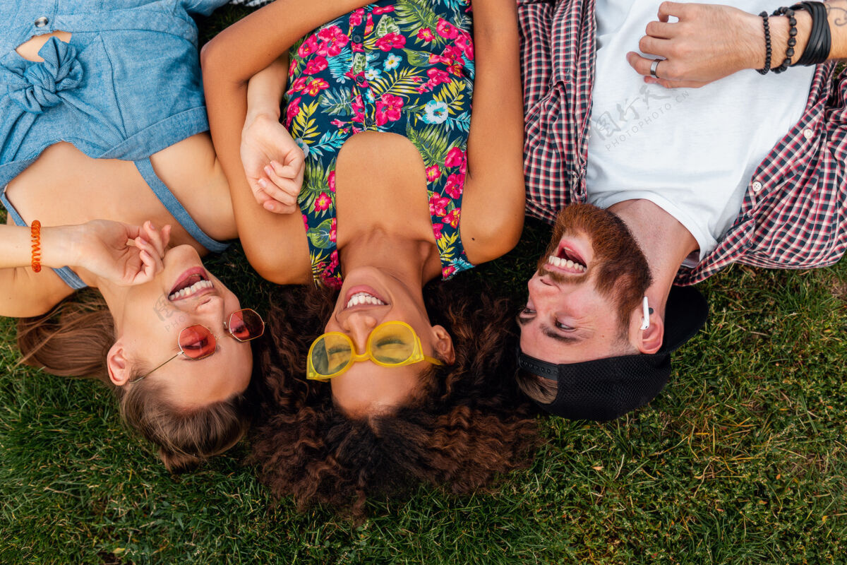 团体俯瞰五颜六色时尚快乐的年轻朋友们躺在公园的草地上 男女同乐人酷太阳镜