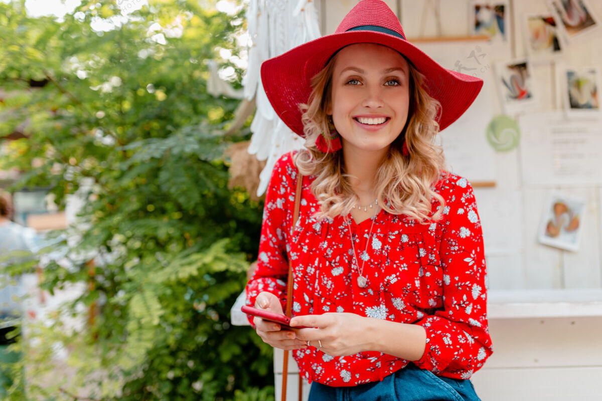 女士迷人的时尚金发微笑的女人在稻草红帽子和衬衫夏季时尚服装举行使用智能手机咖啡厅手机服装女性