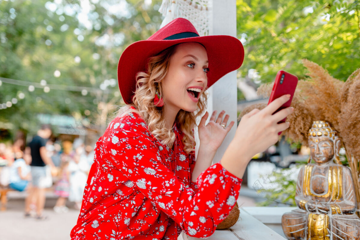 女士迷人的时尚金发微笑的女人在稻草红帽子和衬衫夏季时尚服装举行使用智能手机咖啡厅女性脸手机