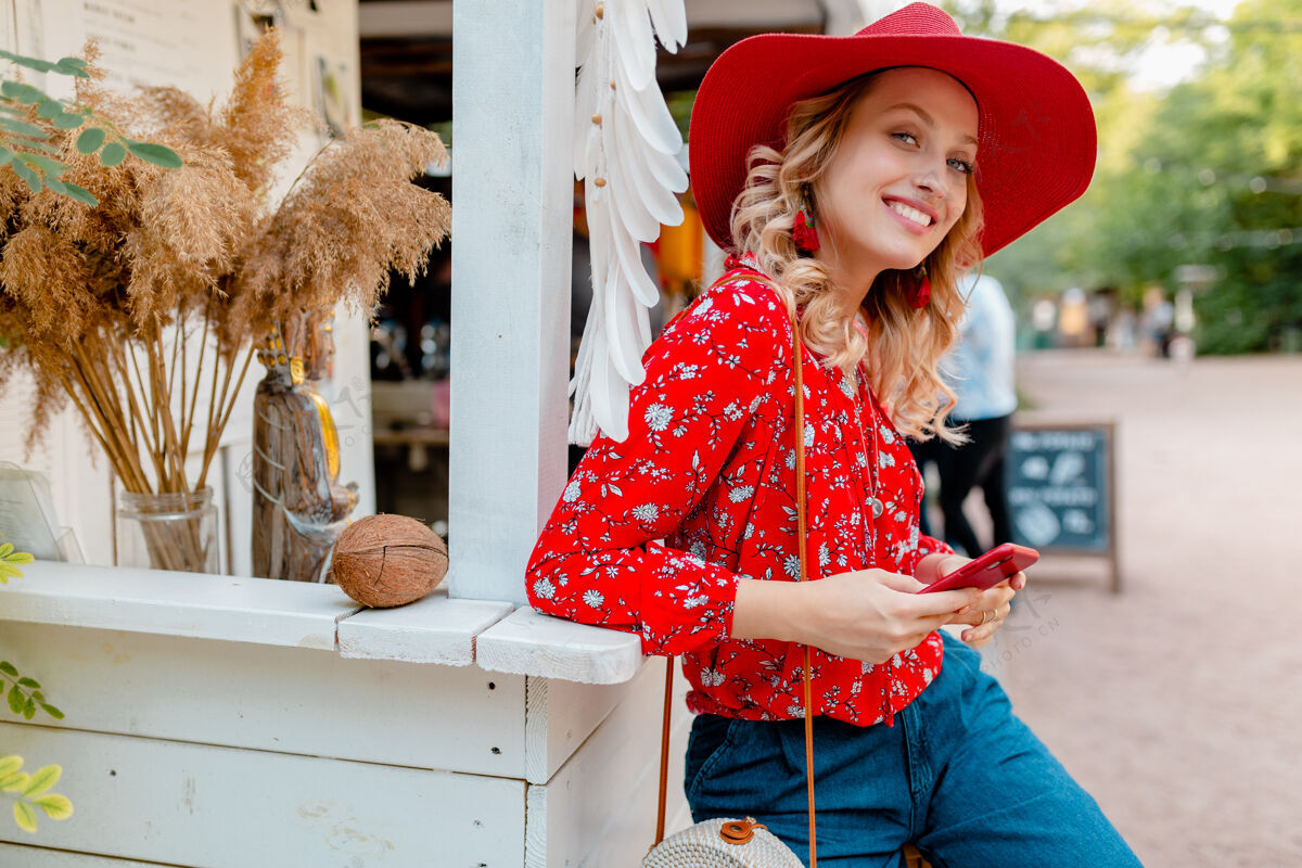 时尚迷人的时尚金发微笑的女人在稻草红帽子和衬衫夏季时尚服装举行使用智能手机咖啡厅女性电话金发