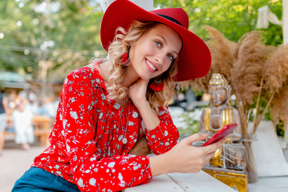 外表迷人的时尚金发微笑的女人在稻草红帽子和衬衫夏季时尚服装举行使用智能手机咖啡厅脸女士情感
