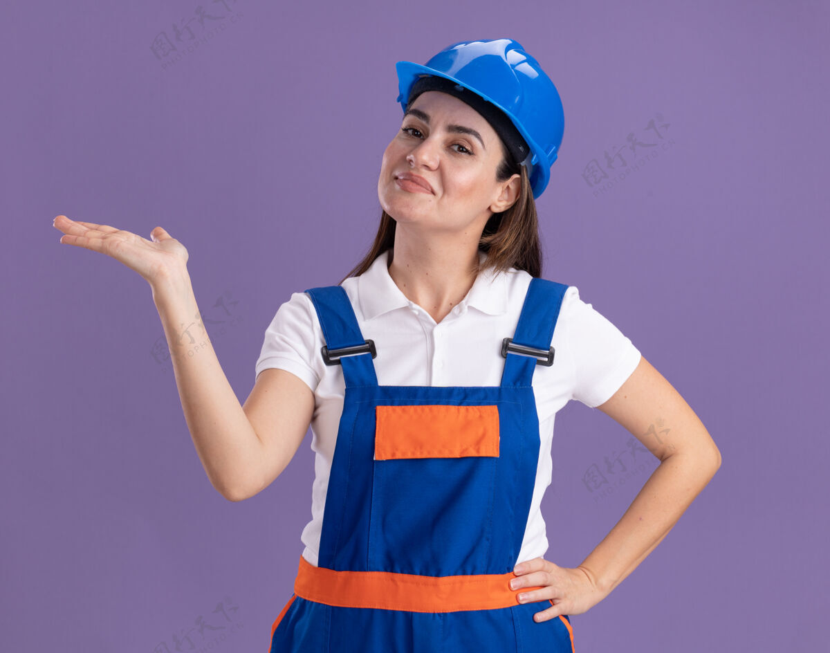 请假装一个穿着制服的年轻建筑工人假装拿着一个孤立的东西在紫色的墙上拿着什么建筑工人女人