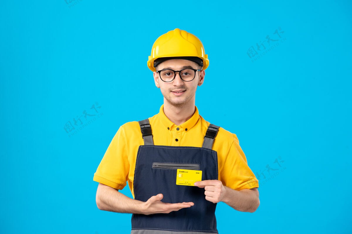 男人蓝色墙壁上穿着制服 手里拿着银行卡的男建筑工人的正视图信用卡前台银行