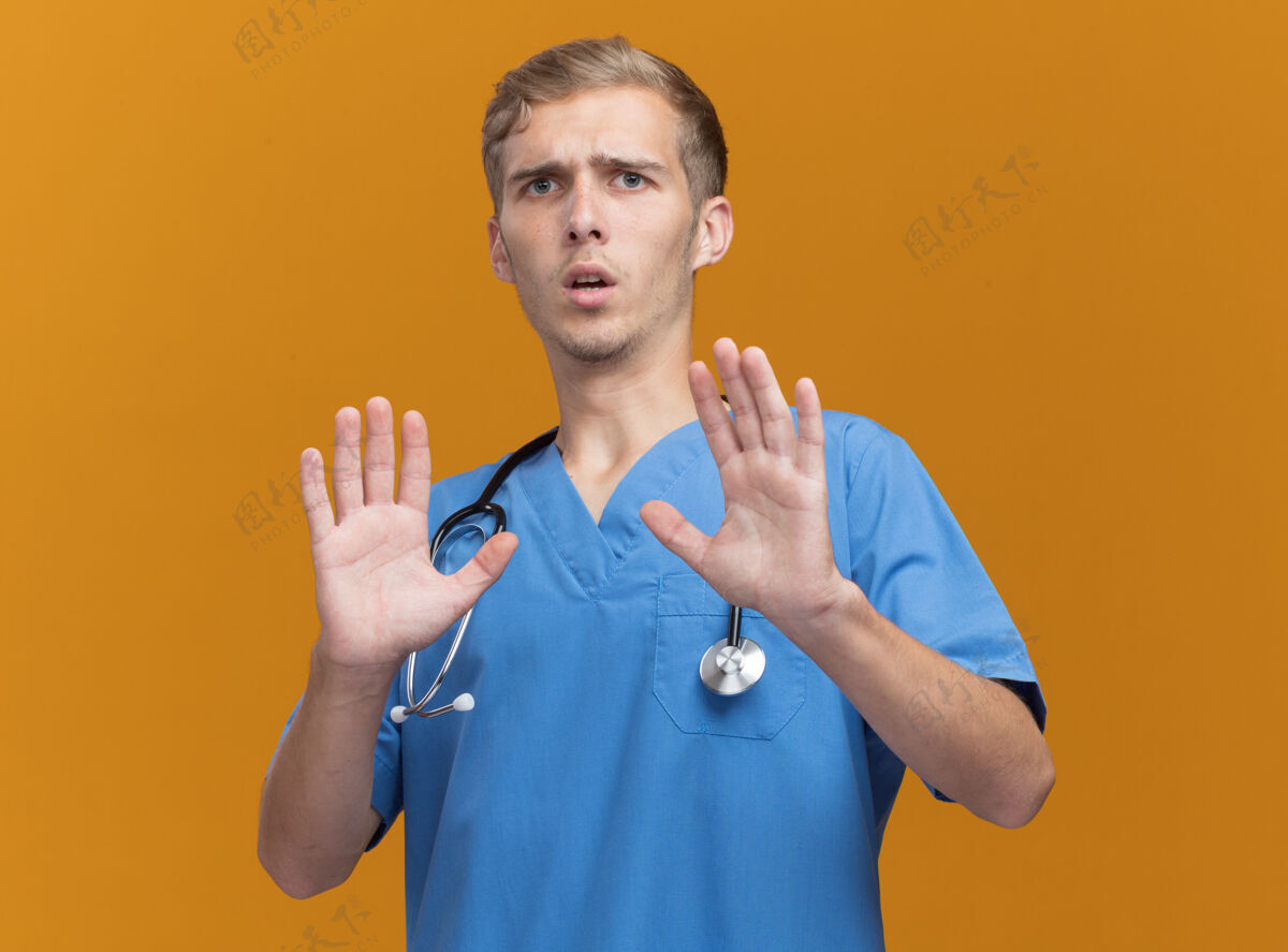 男性被吓坏了的年轻男医生穿着医生制服 听诊器被隔离在橙色的墙上医生年轻听诊器