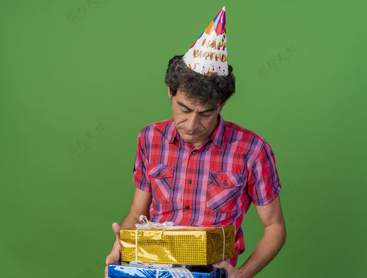 人悲伤的中年白种人聚会男子戴着生日帽 拿着礼物包 看着绿色背景上的复制空间孤立复制生日举行