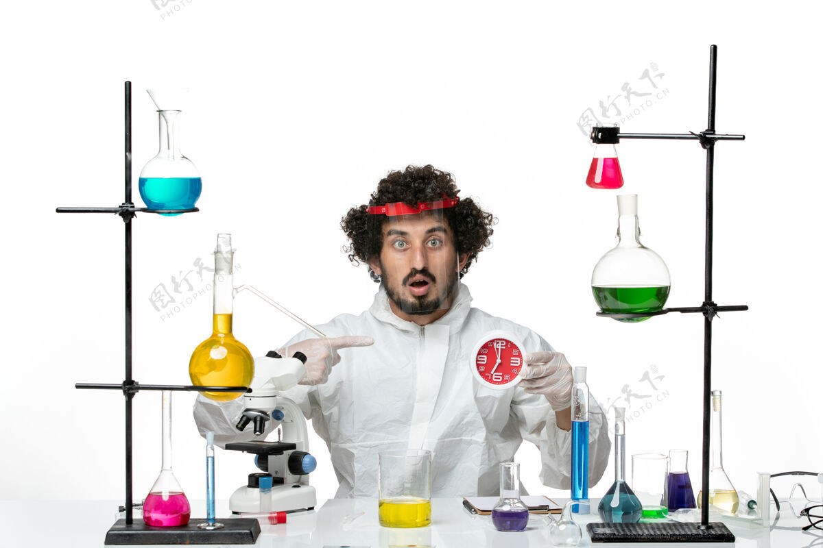 实验室正面图：年轻的男科学家穿着特殊的衣服 戴着防护头盔 在白色的墙上拿着钟头盔医生套装