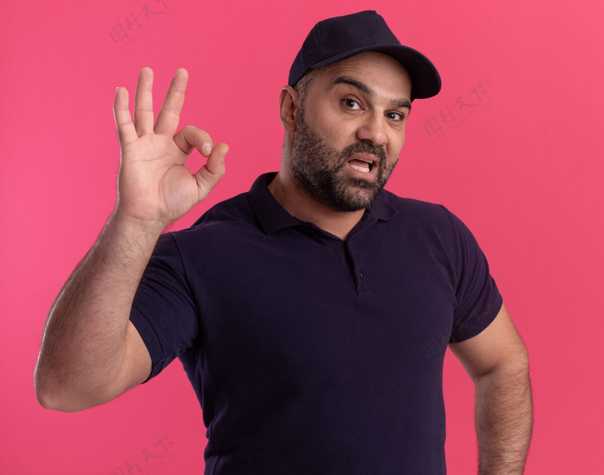 男人自信的中年送货员穿着制服 戴着帽子 在粉红色的墙上显示出良好的姿态好的中年送货