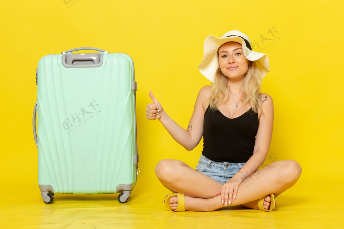 年轻人正面图年轻的女性和她的绿色袋子一起坐在黄墙上旅行度假阳光旅行旅行女孩一路走来成年人漂亮的