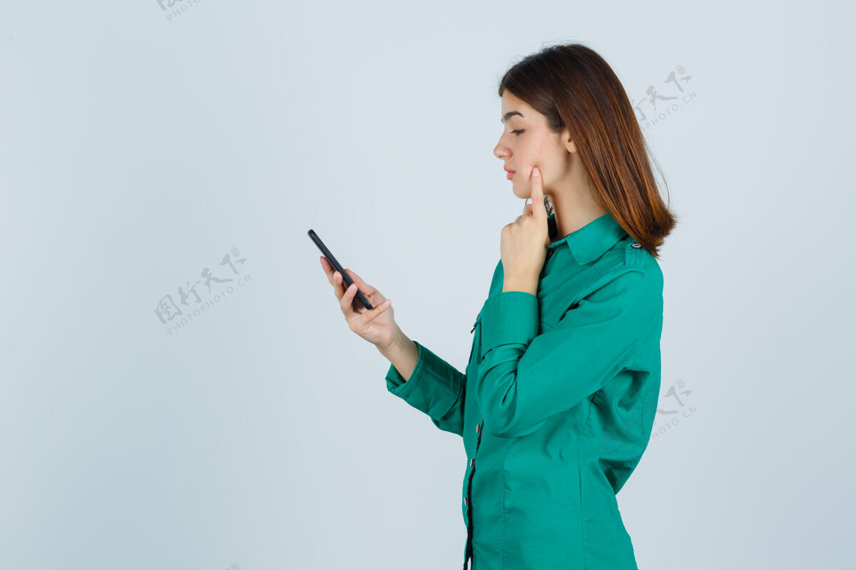 室内穿着绿色上衣 黑色裤子的年轻女孩在看电话留言 把食指放在脸颊上 看起来很专注 前视图电脑课女人儿童后代