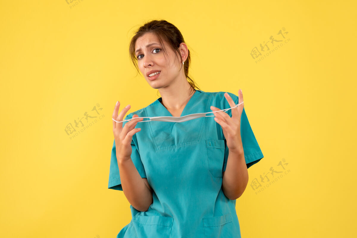 人正面图身着医用衬衫的女医生正在取下黄色背景上的无菌口罩大流行黄色视图