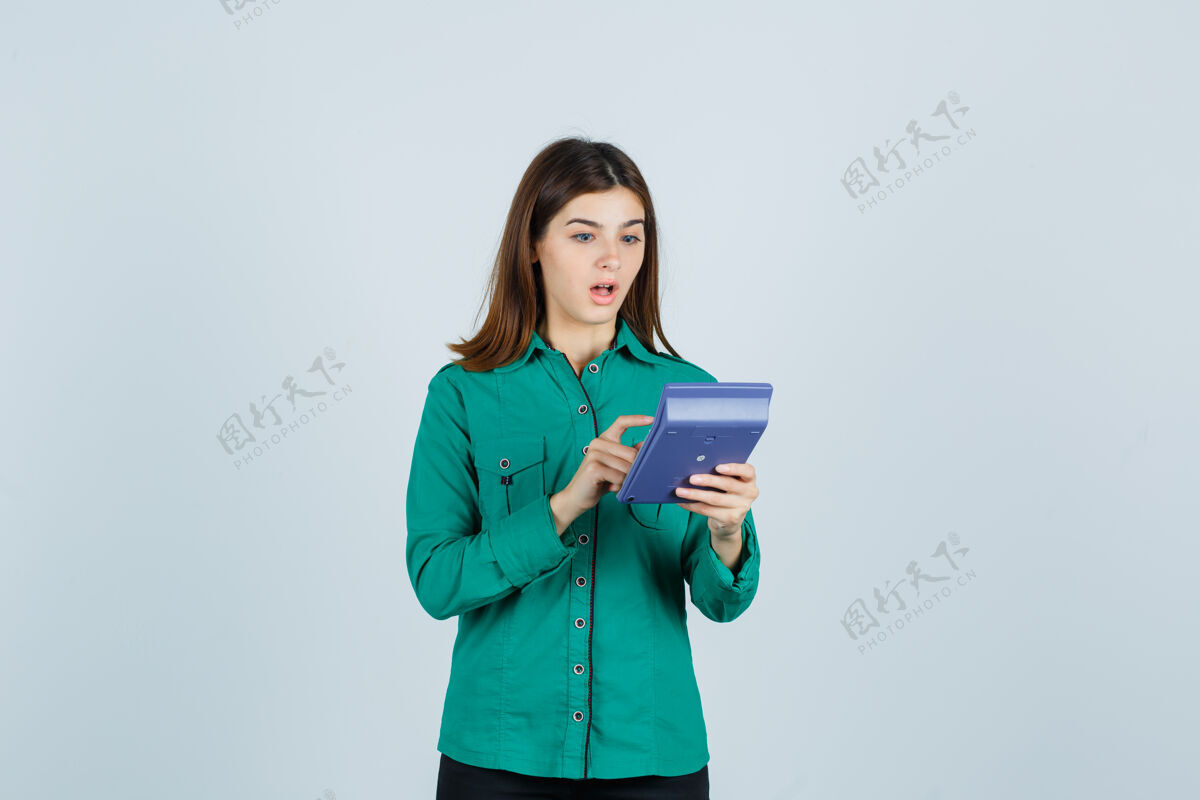 现代穿着绿衬衫的年轻女士正在计算器上做计算 她很好奇地看着前面的景色前面微笑人