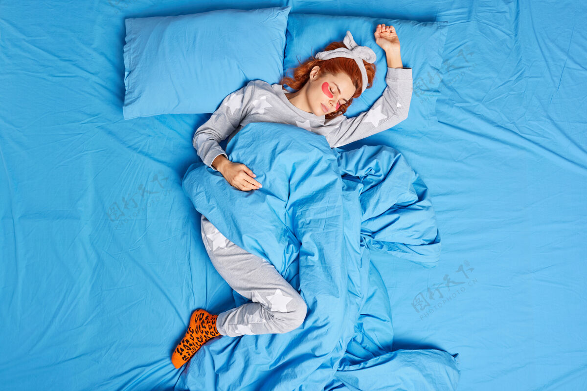 睡眠上图：穿着睡衣头带的放松红发女子睡前在眼睛下敷上美容巾 以减少浮肿 在舒适的床上摆出懒散的姿势宁静的气氛谎言生姜周末